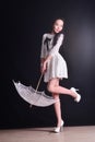 Young slim model in light summer dress with a filigree umbrella posing in studio. Black background