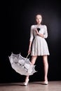 Young slim model in light summer dress with a filigree umbrella posing in studio. Black background Royalty Free Stock Photo