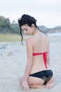 Young slim pretty lady wear red and black bikini sitting on the legs on the sand