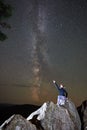 Woman sitting at night alone on top of huge boulder under dark starry summer sky