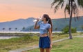 Young slim woman drinking water after exercises and sport against sunset and beach with palms Royalty Free Stock Photo