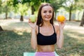 Young slim woman having snack after working out outdoors in the park. Sitting on the grass, eating juicy apple on fresh air