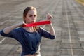 Young slim woman in sportswear doing squats exercise with rubber band on a black coated stadium track