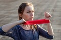 Young slim woman in sportswear doing squats exercise with rubber band on a black coated stadium track