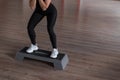 Young slim woman in sporty leggings in a black top in training in a gym crouches using a platform step. Girl coach shows exercises Royalty Free Stock Photo