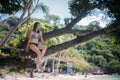 Young slim woman on a tree on the ocean coast on a tropical island on a sunny day