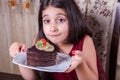 Young small beautiful middle eastern child girl with chocolate cake with pineapple, strawberry, and milk with red dress and dark Royalty Free Stock Photo