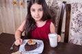 Young small beautiful middle eastern child girl with chocolate cake with pineapple, strawberry, and milk with red dress and dark Royalty Free Stock Photo