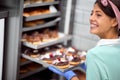 A young small business female owner in a candy workshop posing in front of the closet full of delicious handmade donuts. Pastry,