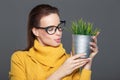 Young smart woman in eyeglasses holding indoor plant in metal po
