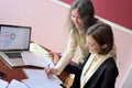 Young smartly dressed lady helps another young lady to work with documents, fill forms and sign. They sit together in a vintage