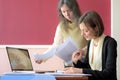 Young smartly dressed lady helps another young lady to work with documents, fill forms and sign