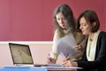 Young smartly dressed lady helps another young lady to work with documents, fill forms and sign Royalty Free Stock Photo