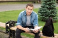 Young smile man reading book while sit on bench at university campus. Happy Man study remotely. Adult student reading in park Royalty Free Stock Photo