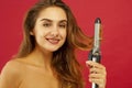 Young smiley woman making curly hair by ploy over red background