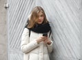 Young smiling adorable woman texting on smartphone posing against grey wooden garage doors. Lifestyle positive emotions concept. Royalty Free Stock Photo