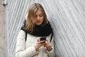 Young smiling adorable woman texting on smartphone posing against grey wooden garage doors. Lifestyle positive emotions concept. Royalty Free Stock Photo