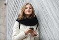 Young smiling adorable woman texting on smartphone posing against grey wooden garage doors. Lifestyle positive emotions concept. Royalty Free Stock Photo