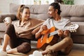 Young smiling african american man musician playing instrumental music on guitar for happy girlfriend