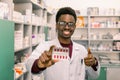 Young smiling African American man pharmacist holding red pills blister in hand while standing in interior of modern Royalty Free Stock Photo