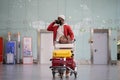 Smiling Black man pushing luggage trolley walking after arrival at airport, talking on mobile phone. Royalty Free Stock Photo