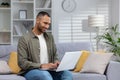 A young smiling African-American man is sitting on a sofa and using a laptop, spending free time on the Internet Royalty Free Stock Photo