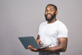 Young smiling african american man standing and using laptop computer isolated over grey background