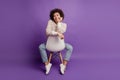 Young smiling african girl hand chik sit chair posing wear casual outfit on purple background