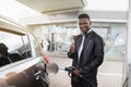 Young smiling African man refuelling his modern car at a petrol station, posing to camera with his thumb up