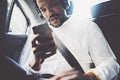 Young smiling african man using smartphone while sitting on backseat in car.Concept of happy business people traveling Royalty Free Stock Photo