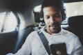 Young smiling african man using smartphone while sitting on backseat in taxi car.Concept of business people traveling Royalty Free Stock Photo