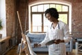 African woman painter holding palette painting on canvas in workshop