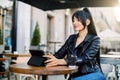 Young smiling Asian brunette girl with ponytail hair, using digital tablet for work while sitting at outdoor cafe Royalty Free Stock Photo