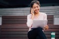 Young smiling Asian girl using a mobile phone and laptop on her lap in university campus building Royalty Free Stock Photo