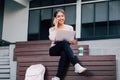 Young smiling Asian girl using a mobile phone and laptop on her lap in university campus building Royalty Free Stock Photo