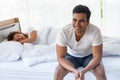 Young smiling Asian man sitting on bed while his unhappy girlfriend sleeping on bed Royalty Free Stock Photo