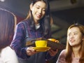 Young smiling asian waitress serving coffee to customers