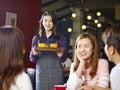 Young smiling asian waitress serving coffee to customers