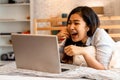 Young smiling Asian woman in casual clothing and lying on bed with laptop computer. Female freelancer working from home Royalty Free Stock Photo