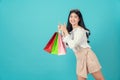 Young smiling asian woman holding multi coloured shopping bags and hands pointing finger on light blue background. Royalty Free Stock Photo