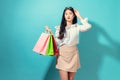 Young smiling asian woman holding multi coloured shopping bags and hands touch the glasses on light blue background. Royalty Free Stock Photo