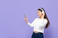 Young smiling Asian woman listening to music on mobile phone using wireless headphone in purple  studio Royalty Free Stock Photo