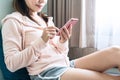 Young smiling Asian woman sitting on sofa and using mobile phone. Young brunette girl relaxing at home in a leisure time Royalty Free Stock Photo