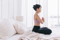 Young smiling attractive sporty Asian woman practicing yoga on the bed, doing Ardha Padmasana exercise, meditating in Half Lotus Royalty Free Stock Photo