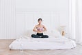 Young smiling attractive sporty Asian woman practicing yoga on the bed, doing Ardha Padmasana exercise. Royalty Free Stock Photo