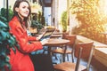 Young smiling attractive woman in orange coat is sitting outside in cafe at table and uses tablet computer. Royalty Free Stock Photo