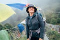 Young smiling backpacker woman crossing canyon over Suspension Bridge with multicolored Tibetan Prayer flags. Mera peak climbing Royalty Free Stock Photo