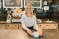 Young smiling barista girl with cup of freshly prepared coffee. Blond woman in an apron, near the bar counter in coffee shop Royalty Free Stock Photo