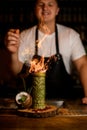 Young smiling bartender sprinkles cinnamon on burning alcohol drink