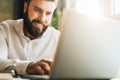 Young smiling bearded businessman sitting in office at table, using laptop. Man works on computer, checks e-mail. Royalty Free Stock Photo